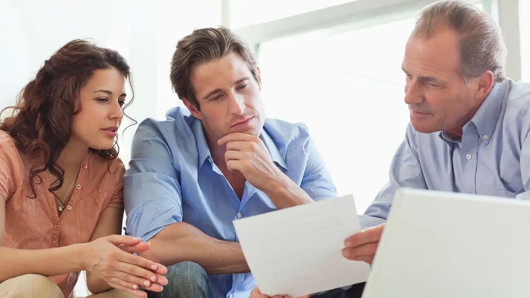 A couple reviewing documents and a laptop with a mortgage adviser.