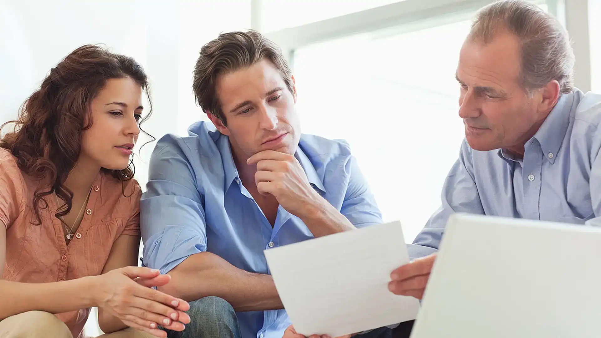 A couple reviewing documents and a laptop with a mortgage adviser.